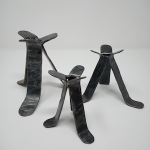 May include: Three black metal candle holders with a unique, three-legged design. The holders are made of forged metal and have a rustic, industrial look.