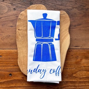 Pode incluir: Toalha de cozinha branca com uma ilustração azul de uma cafeteira e o texto "Sunday Coffee".