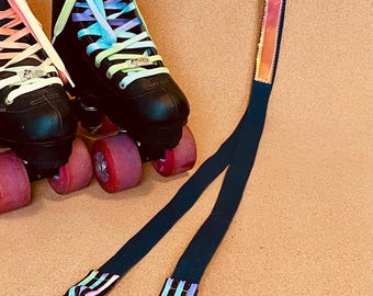 Puede incluir: Patines negros con cordones coloridos y ruedas rosas están junto a una correa de transporte verde azulado con detalles reflectantes y mosquetones azules. La correa está diseñada para transportar los patines. El fondo es una superficie marrón claro.