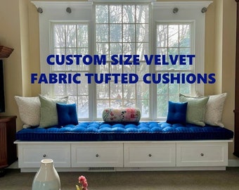 May include: A long, rectangular, deep blue velvet tufted bench cushion sits on a white window seat with drawers. The cushion is accented by two square blue pillows, two light green pillows, two patterned pillows, and a floral bolster pillow. Text reads: CUSTOM SIZE VELVET FABRIC TUFTED CUSHIONS.
