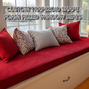 May include: Custom trapezoid shape foam filled window seats featuring a long red textured cushion on a white base with drawers. The arrangement includes two solid red pillows, two patterned red and white pillows, and one solid light gray pillow.