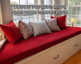 May include: A red window seat with a custom trapezoid shape and foam filled cushions. The seat has a white frame and is decorated with various patterned throw pillows.