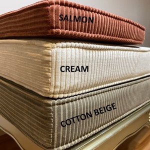 May include: Three corduroy cushion covers stacked on top of each other. The top cover is salmon, the middle cover is cream, and the bottom cover is cotton beige.