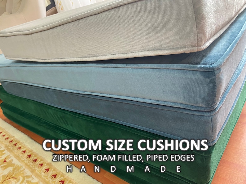 May include: Three custom size cushions in different colours: light grey, blue, and green. The cushions are zippered, foam filled, and have piped edges. The text "CUSTOM SIZE CUSHIONS" and "ZIPPERED, FOAM FILLED, PIPED EDGES" is printed on the green cushion. The text "HANDMADE" is printed below the text on the green cushion.