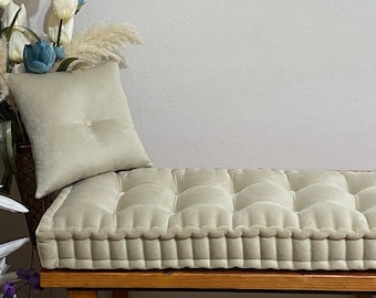 May include: A beige tufted cushion with a button detail sits on a wooden bench. The cushion is made of a soft, plush fabric and has a simple, elegant design.