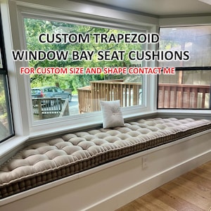 May include: Custom trapezoid window bay seat cushions with tufted upholstery.  The cushions are beige and are placed on a white window seat.  "FOR CUSTOM SIZE AND SHAPE CONTACT ME" is written in red text on the window.