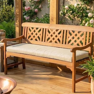 May include: Wooden outdoor bench with a lattice back design and curved armrests. The bench features a beige cushion and is surrounded by greenery. A small side table is visible to the left.