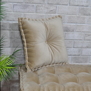 May include: A beige tufted cushion with a beige velvet pillow on top. The pillow has a button detail in the center.
