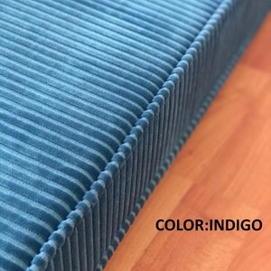 May include: Close-up of a blue corduroy fabric with a stitched edge. The fabric has a ribbed texture and is a deep indigo color. COLOR: INDIGO