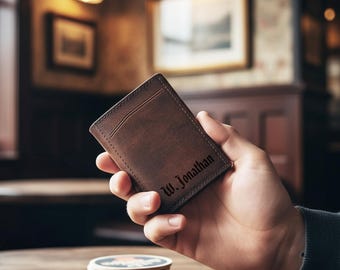 Może przedstawiać: Brązowy skórzany etui na karty z wygrawerowanym imieniem "W. Jonathan". Etui na karty ma smukłą konstrukcję z kieszenią z przodu. Tło to rozmyte wnętrze z ciepłym oświetleniem.
