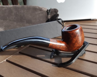 May include: A brown wooden pipe with a black stem and a black stand. The pipe is sitting on a wooden table.