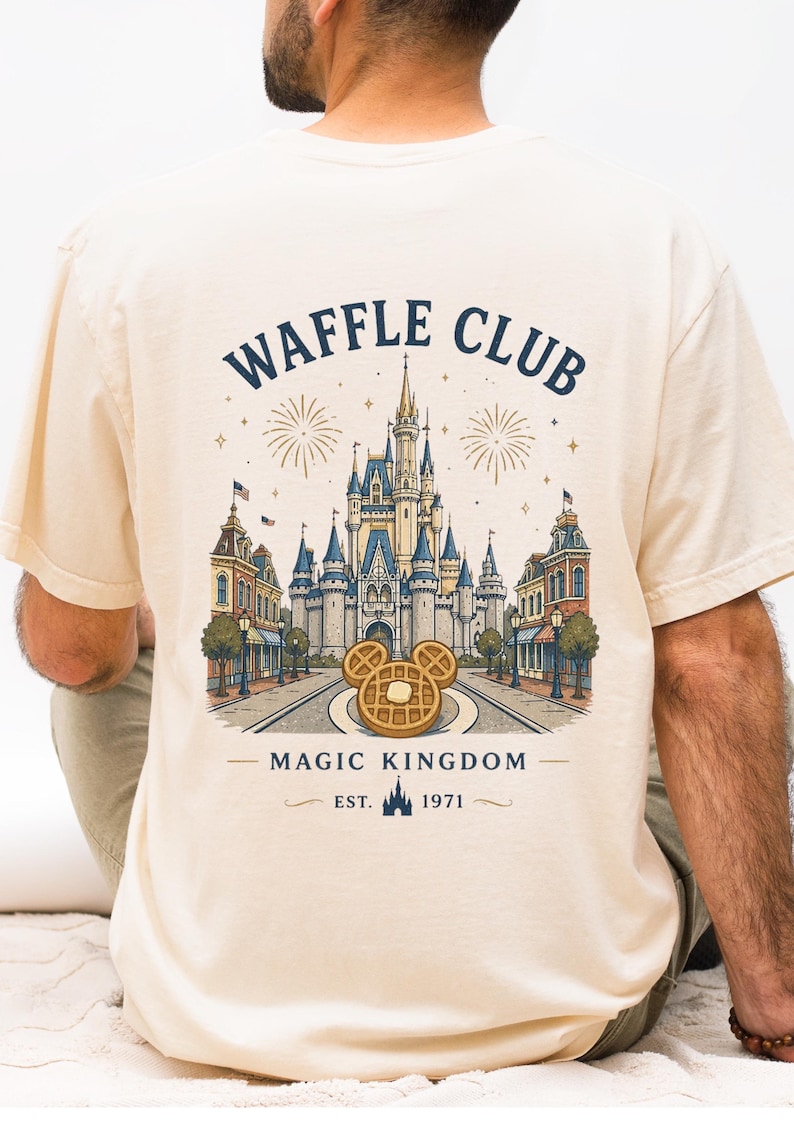 K&ouml;nnte beinhalten: Cremefarbenes T-Shirt mit einem Aufdruck von Cinderella's Schloss, Feuerwerk und einem Waffeldesign mit Mickey Mouse Ohren. Der Text lautet "WAFFLE CLUB" und "MAGIC KINGDOM EST. 1971".