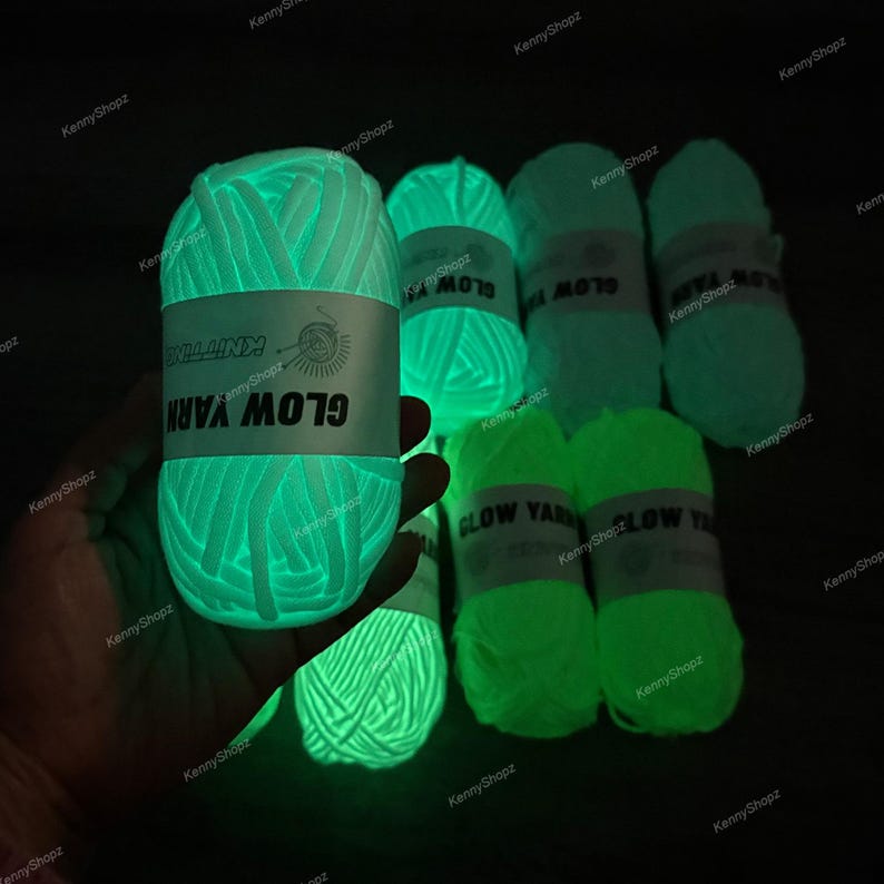 May include: Several skeins of glow-in-the-dark yarn emitting a bright neon green light in a dark environment. Each skein features a white paper label with the text GLOW YARN and a small knitting icon. The yarn has a thick, soft texture.