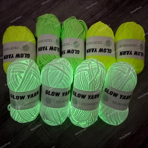 May include: Eight skeins of glow-in-the-dark yarn arranged in two rows. The top row features four skeins of neon yellow yarn, while the bottom row displays four skeins of white yarn. Each skein has a white paper label printed with GLOW YARN.