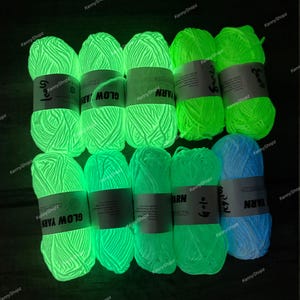 May include: Ten skeins of glow-in-the-dark yarn arranged in two rows. Each skein features a white paper label with the text GLOW YARN printed on it. The yarn emits a bright neon green light, except for one skein on the bottom right which glows blue.