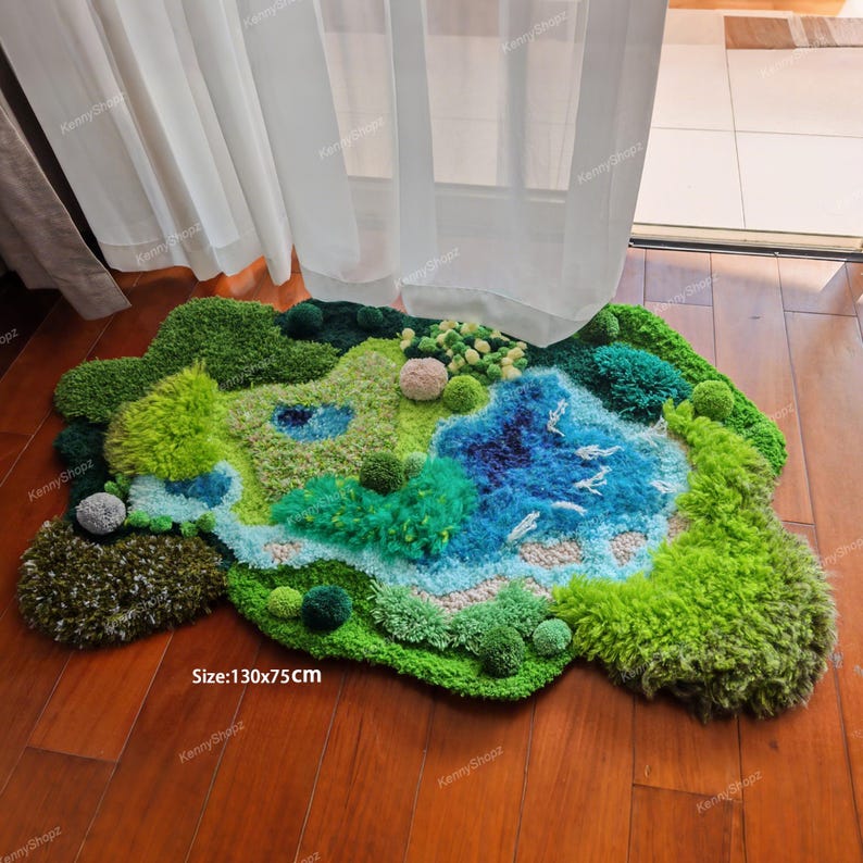 K&ouml;nnte beinhalten: Ein getufteter Teppich mit unregelm&auml;&szlig;iger Form, der eine Landschaft mit gr&uuml;nen H&uuml;geln, einem blauen See und kleinen texturierten Pompons zeigt. Der Teppich weist verschiedene Gr&uuml;n- und Blaut&ouml;ne auf und tr&auml;gt die Gr&ouml;&szlig;enangabe 130x75CM.