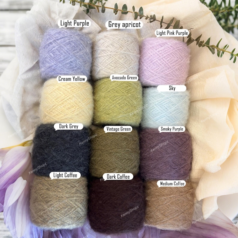 May include: Twelve balls of fuzzy yarn arranged in a grid, labeled with colors: Light Purple, Grey apricot, Light Pink Purple, Cream Yellow, Avocado Green, Sky, Dark Grey, Vintage Green, Smoky Purple, Light Coffee, Dark Coffee, and Medium Coffee.