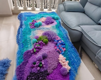 Puede incluir: Una alfombra rectangular con mechones que presenta una superficie texturizada con alturas de pelo variables en tonos azul, morado, verde azulado, verde y rosa pálido. El diseño incorpora pompones y formas con mechones sobre una malla.