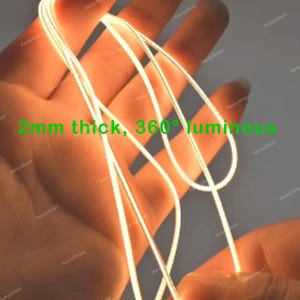 May include: A flexible, thin, glowing light wire with a 2mm thickness and 360-degree luminous output. The cord emits a bright, warm light and is shown looped in a continuous strand, featuring the printed text 2mm thick, 360&deg; luminous.