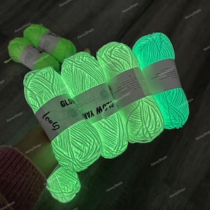 May include: Several skeins of neon green glow-in-the-dark yarn, each wrapped with a white paper label featuring the text "GLOW YARN" and "KNITTING". The yarn emits a bright, luminous light, showcasing its phosphorescent properties in a dark setting.