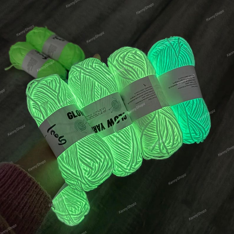 May include: Several skeins of neon green glow-in-the-dark yarn, each wrapped with a white paper label featuring the text "GLOW YARN" and "KNITTING". The yarn emits a bright, luminous light, showcasing its phosphorescent properties in a dark setting.