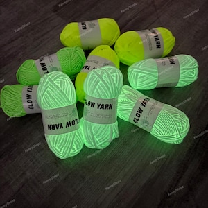 May include: A collection of neon yellow yarn skeins that glow in the dark. Each skein is wrapped in a white paper band featuring the black text GLOW YARN KNITTING. The yarn has a thick, textured appearance and is arranged in a scattered group.