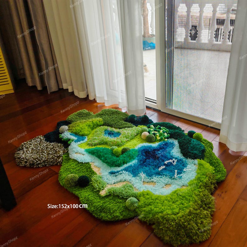 K&ouml;nnte beinhalten: Ein unregelm&auml;&szlig;iger, getufteter Teppich mit einer Landschaftsdarstellung in Gr&uuml;n-, Blau- und Braunt&ouml;nen. Der Teppich zeigt eine topografische Szene mit einem zentralen blauen See, Grasfl&auml;chen und strukturierten Waldst&uuml;cken. Der Text lautet Size:152x100 cm.
