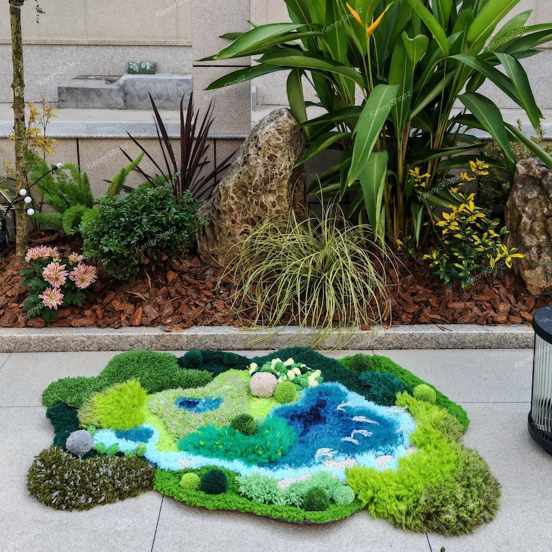 K&ouml;nnte beinhalten: Ein getufteter Teppich mit einem abstrakten Landschaftsmotiv aus verschiedenfarbigen gr&uuml;nen, blauen und wei&szlig;en Garnen. Der Teppich hat eine moosartige Textur mit erhabenen, kreisf&ouml;rmigen B&uuml;scheln und einem geschwungenen blauen Flussmuster.