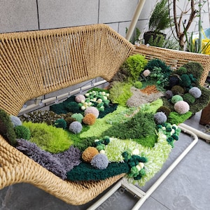May include: A green, brown, and white rug with pom-poms is placed on a woven wicker swing chair. The rug is made of yarn and has a textured, fluffy surface.