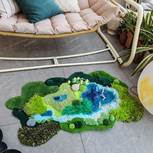 K&ouml;nnte beinhalten: Ein getufteter Teppich mit einem abstrakten Landschaftsdesign in verschiedenen Texturen und Schattierungen von Gr&uuml;n, Blau und Wei&szlig;. Der Teppich zeigt ein topografisches Muster mit erhabenen B&uuml;scheln, die H&uuml;gel, Wasser und Vegetation darstellen.