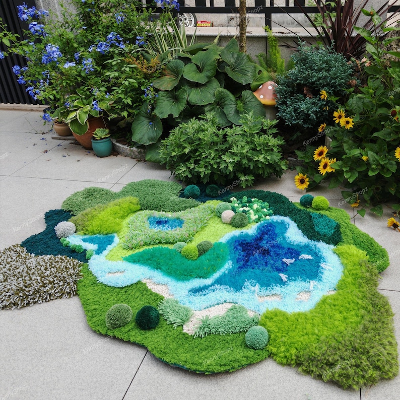 K&ouml;nnte beinhalten: Ein getufteter Teppich mit einem abstrakten Landschaftsmotiv aus verschiedenfarbigen gr&uuml;nen, blauen und wei&szlig;en Garnen. Der Teppich hat eine unregelm&auml;&szlig;ige, organische Form mit texturierten Florh&ouml;hen und stellt ein Gew&auml;sser dar.