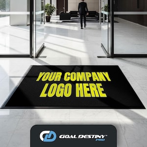 May include: Black rectangular welcome mat with the text "YOUR COMPANY LOGO HERE" in yellow. The mat is placed in front of glass doors in a commercial building. The Goal Destiny Pro logo is in the bottom right corner.