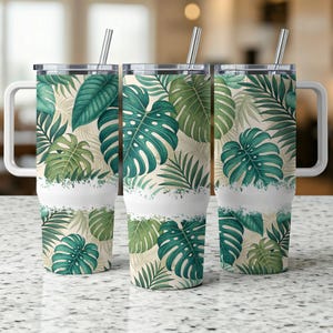 Könnte beinhalten: Drei Edelstahlbecher mit tropischem Blattdesign. Die Becher haben einen weißen Streifen um die Mitte und einen Deckel mit einem Strohhalm.