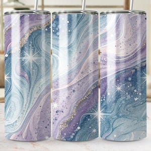 Peut inclure: Trois gobelets en acier inoxydable avec un motif tourbillonnant à l'aquarelle dans les tons de bleu, violet et blanc, agrémenté de paillettes argentées et d'étoiles. Chaque gobelet a une paille argentée.