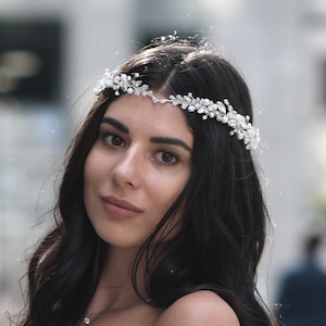 Puede incluir: Una mujer con el pelo largo y oscuro que lleva un vestido blanco de hombros descubiertos y una diadema plateada con detalles de perlas.