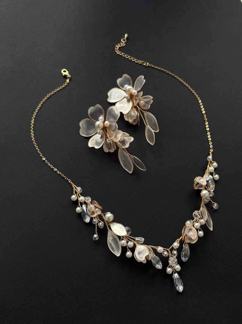 K&ouml;nnte beinhalten: Ein zarte goldfarbene Halskette und ein passendes Ohrring-Set. Der Schmuck verf&uuml;gt &uuml;ber durchscheinende Bl&uuml;ten- und Bl&auml;tterakzente, Kunstperlen und klare, kristallartige Verzierungen. Das Set ist mit einem floralen Thema gestaltet, perfekt f&uuml;r besondere Anl&auml;sse.