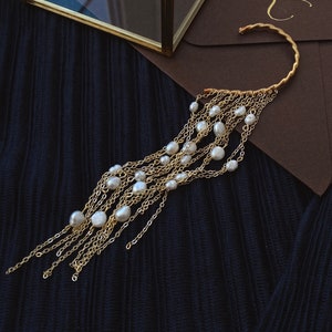 May include: A gold ear cuff with a cascading chain of pearls. The ear cuff is made of wire and has a simple, elegant design. The pearls are white and round, and they are strung on a delicate chain.
