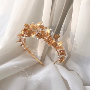 Op de afbeelding: Een gouden bloemenhoofdband met parel accenten. De hoofdband is gevormd als een kroon en is perfect voor een bruiloft of speciale gelegenheid.