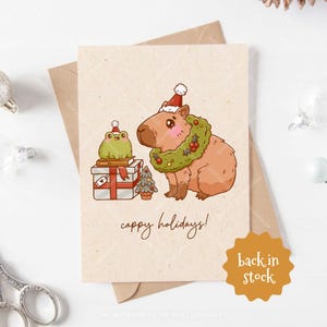 Carte de voeux de Noël Cappy Holidays, Capybara mignon et grenouille avec cadeaux, carte de fête, carte postale A6 vierge pour les fêtes avec enveloppe artisanale