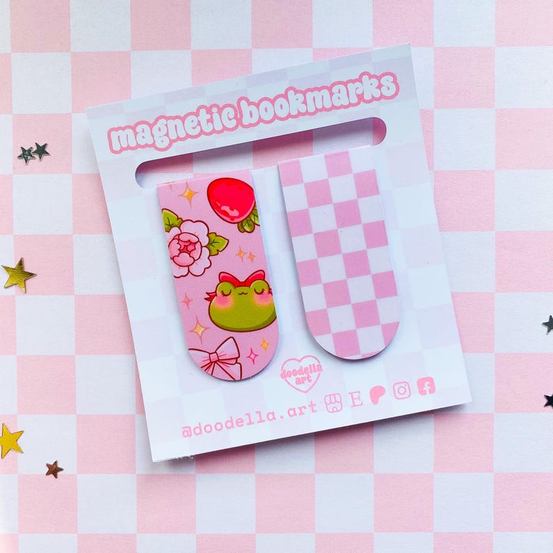 May include: Two magnetic bookmarks on a pink and white checkered background. One bookmark features a frog, flowers, and a bow. The other has a pink and white checkerboard pattern. The words "magnetic bookmarks" are at the top.