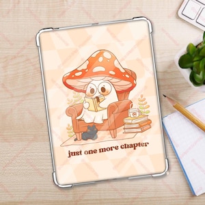 Może przedstawiać: Przezroczyste etui na telefon z uroczą ilustracją ducha czytającego książkę w fotelu w kształcie grzyba. Pod ilustracją znajduje się napis "just one more chapter".