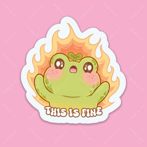 Könnte beinhalten: Ein Aufkleber mit einem Cartoon-Frosch mit großen Augen und rosigen Wangen, umgeben von Flammen. Der Frosch hat einen kleinen Spross auf dem Kopf und der Text "THIS IS FINE" steht darunter. Der Aufkleber hat einen weißen Rand auf rosa Hintergrund.