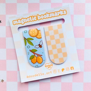 May include: Two magnetic bookmarks on a white card with the text "magnetic bookmarks". One bookmark features lemons, leaves, and a bee on a light blue background. The other has a yellow and white checkerboard pattern. The card has the text "doodella.art".
