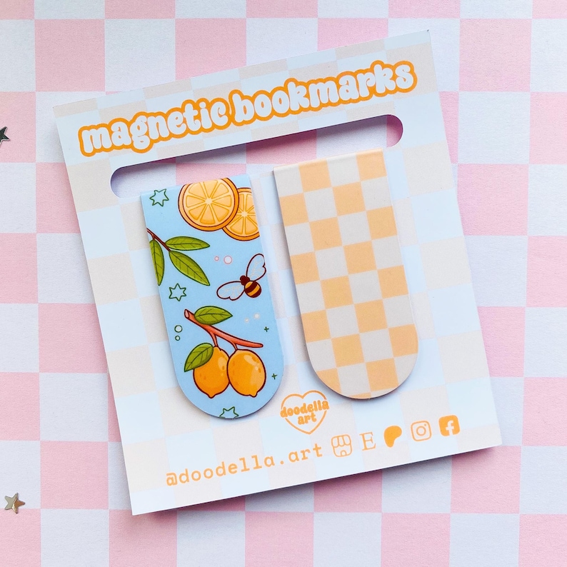 May include: Two magnetic bookmarks on a white card with the text "magnetic bookmarks". One bookmark features lemons, leaves, and a bee on a light blue background. The other has a yellow and white checkerboard pattern. The card has the text "doodella.art".