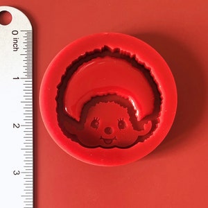 Könnte beinhalten: Rote Silikonform zum Herstellen von Kunsthandwerk aus Harz. Die Form zeigt eine Comicfigur mit einem breiten Lächeln und lockigem Haar.