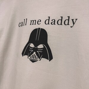 Op de afbeelding: Wit T-shirt met een zwarte afbeelding van Darth Vaders hoofd en de tekst "call me daddy".