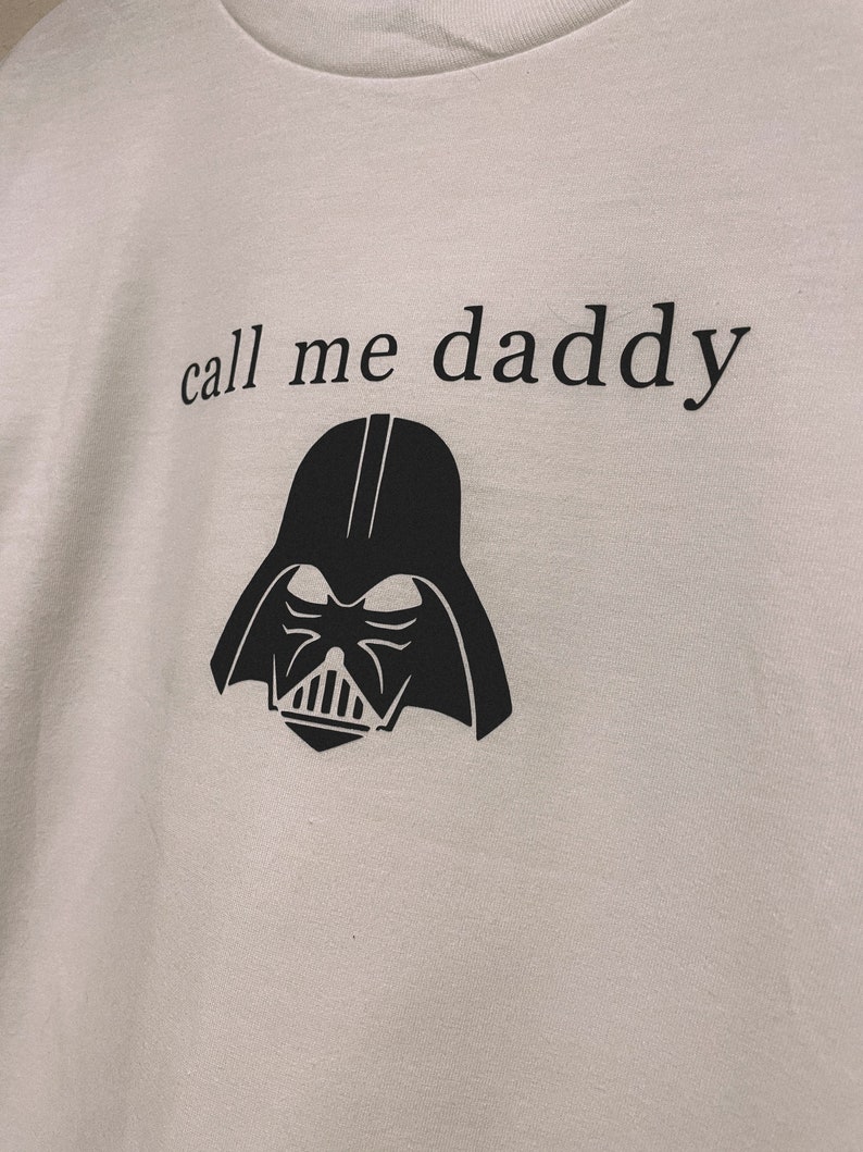 Op de afbeelding: Wit T-shirt met een zwarte afbeelding van Darth Vaders hoofd en de tekst "call me daddy".