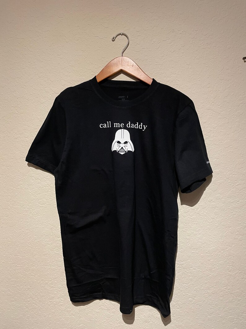 Op de afbeelding: Zwart T-shirt met een witte afbeelding van Darth Vaders helm en de tekst "call me daddy".
