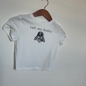 Op de afbeelding: Wit kort T-shirt met een zwart-witte illustratie van Darth Vaders hoofd en de tekst "call me daddy".