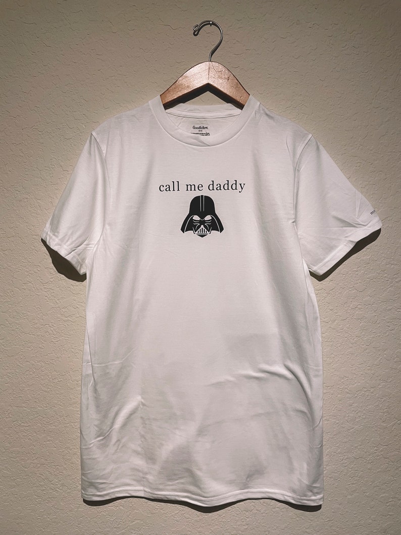 Op de afbeelding: Wit T-shirt met een zwarte Darth Vader-afbeelding en de tekst "call me daddy" gedrukt op de voorkant.